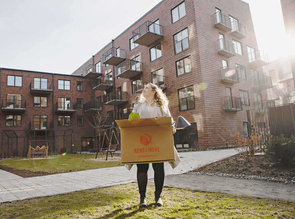 En kvinna står utanför bostadsrättsföreningen Blanka hållandes en flyttkartong.